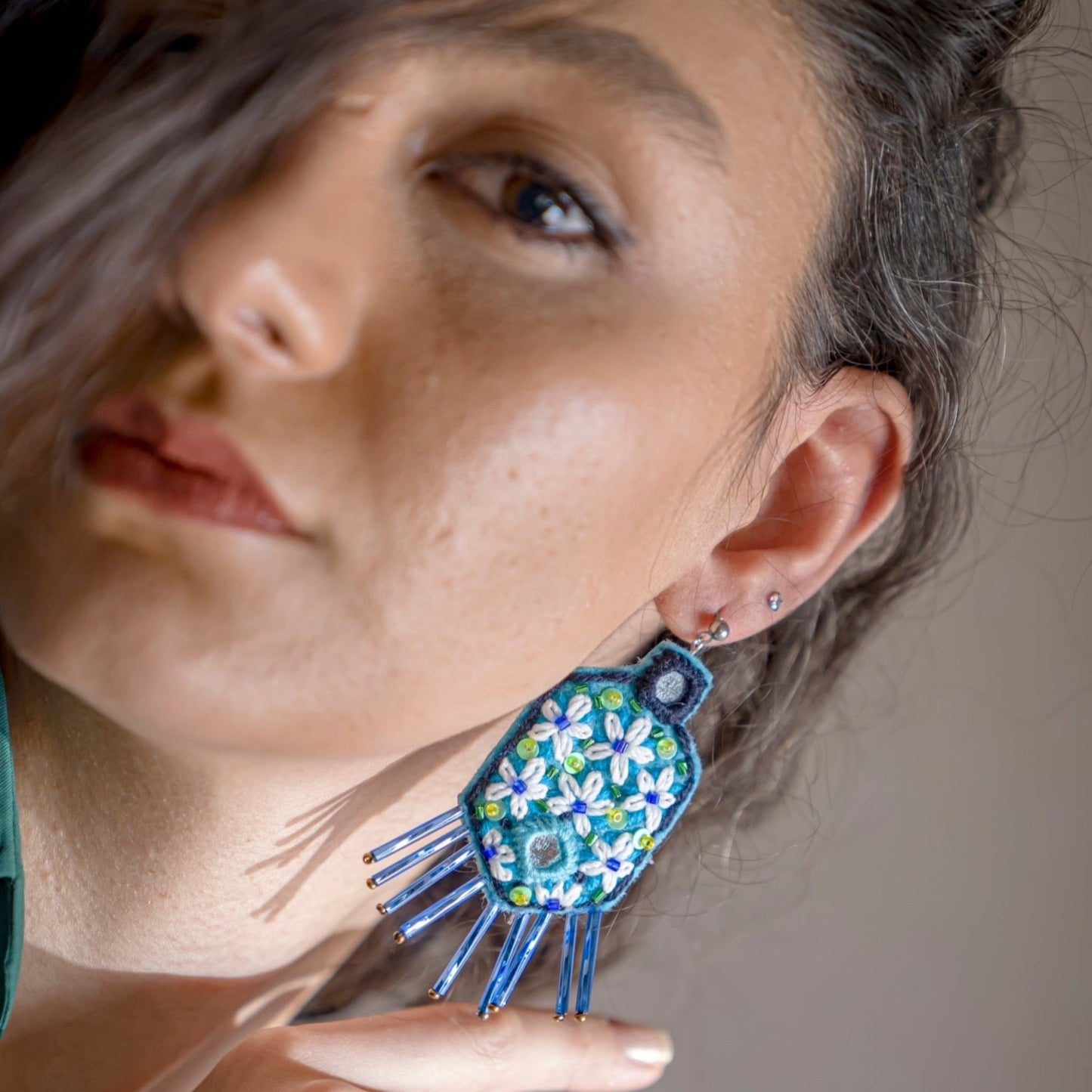 Nature-inspired hand-embroidered earrings with intricate floral patterns in blue and green, embellished with delicate beadwork.